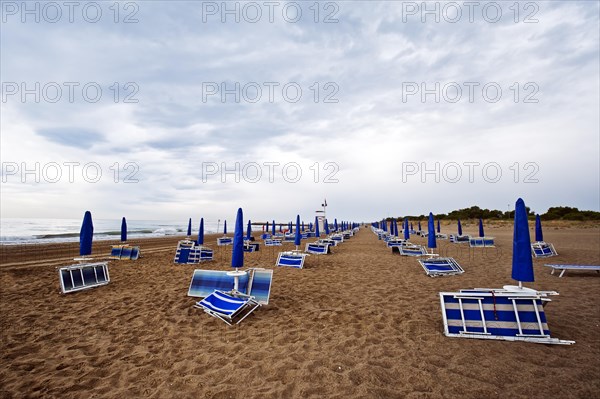 Folded deck chairs and parasols on a beach by the sea with rain clouds