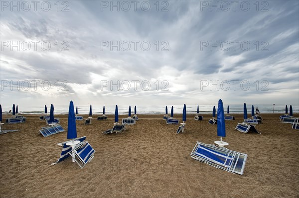 Folded deck chairs and parasols on a beach by the sea with rain clouds