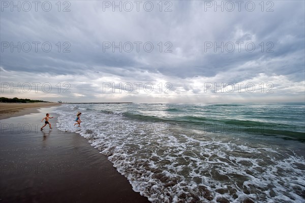 Two children running into the ocean with clouds providing a threatening mood