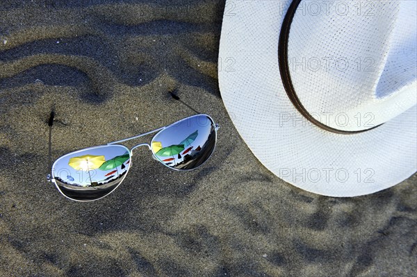 Parasols are reflected in sunglasses lying in the sand