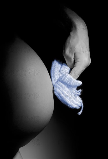 Hand making blue baby shoes walk on a pregnant belly