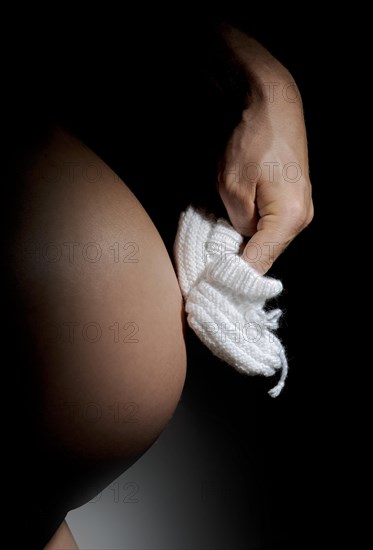 Hand making white baby shoes walk on a pregnant belly
