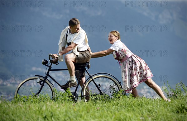 Man and a woman wearing traditional costume with an old bicycle within a natural landscape