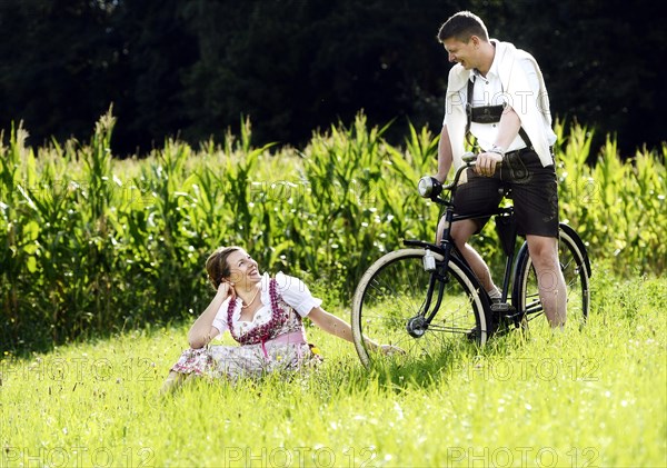 Man and a woman wearing traditional costume with an old bicycle within a natural landscape