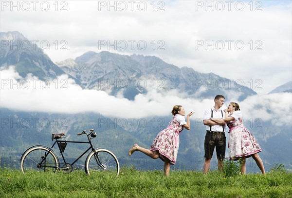 Man and a woman wearing traditional costume with an old bicycle within a natural landscape