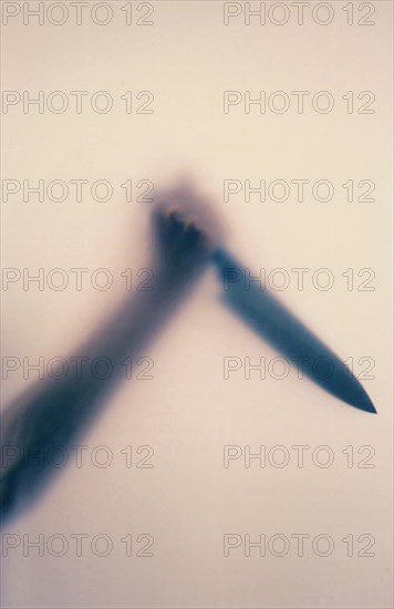 Raised hand holding a large butcher's knife behind frosted glass