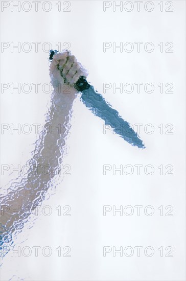 Raised hand holding a large butcher's knife behind cathedral glass
