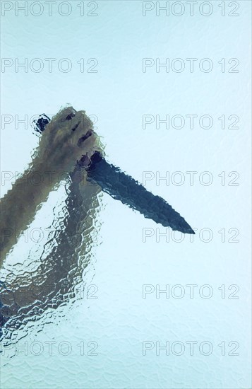 Two raised hands holding a large butcher's knife behind cathedral glass