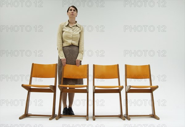 Woman wearing conservative clothes standing behind a row of orange chairs