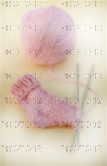 Semi-finished knitted pink baby sock with a ball of wool and knitting needles