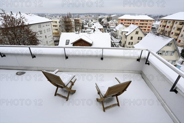 Two snow-covered chairs on a terrace