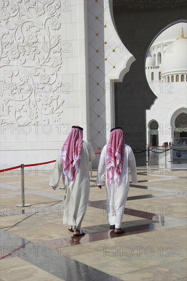 Two men in Arab dress walking in front of the Sheikh Zayed Mosque