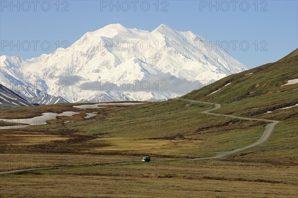 A shuttle bus from the Denali National Park and Preserve crossing the tundra with views of Mt McKinley at back