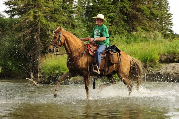 Cowboy riding through a river with splashing water