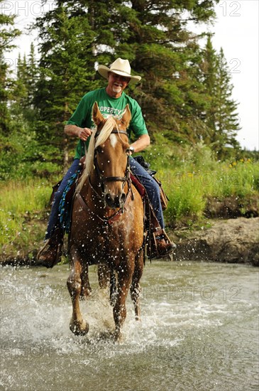 Cowboy riding through a river with splashing water