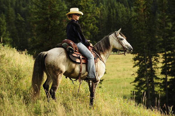 Cowgirl riding a gray horse through the prairie