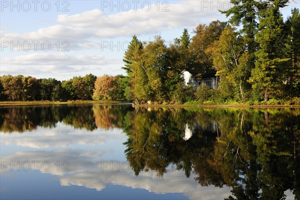 House surrounded by the autumn-coloured forest reflecting in Lake Kamaniskeg