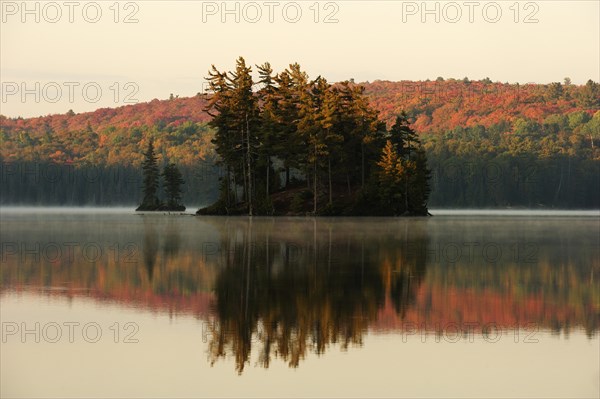 Small island in Thompson Lake and colourful autumnal forest reflected in the water