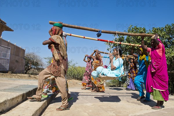 Young Indian women wearing traditional saris carrying long bamboo poles on their heads with a seat for pilgrims climbing the steps to the temple complex