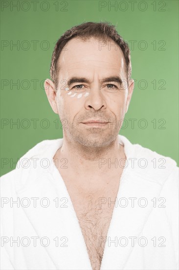 Man wearing a bathrobe with eye cream