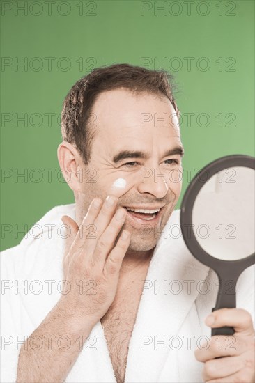 Man wearing a bathrobe looking at himself in a hand mirror