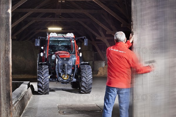 Farmer opening a barn door revealing a tractor behind it