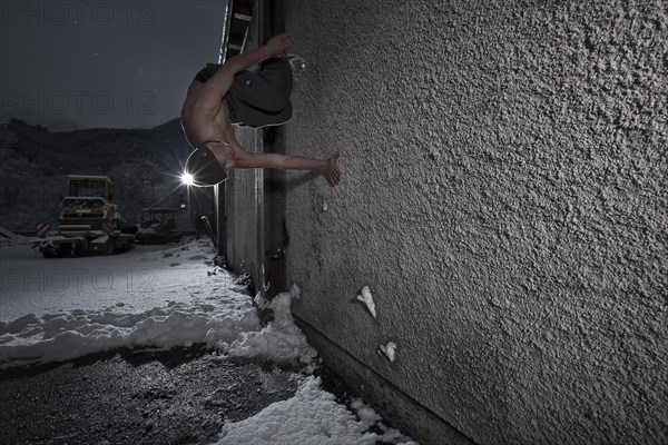 Freerunner doing a somersault on the wall of an old industrial site