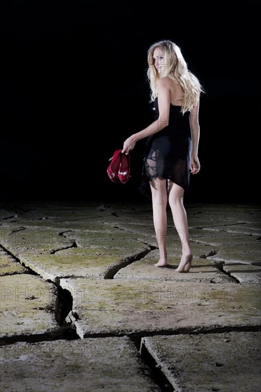 Young woman walking barefoot in an evening dress across cracked clay