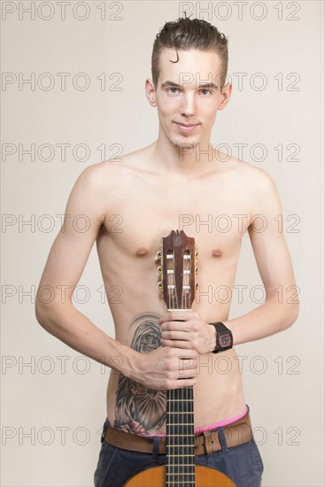 Bare-chested young man with tattoo holding a guitar