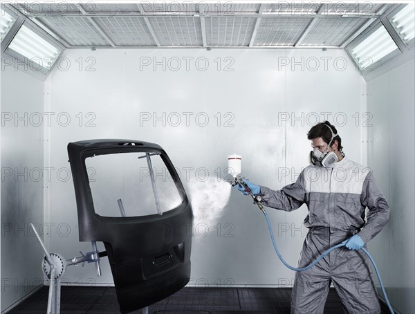 Worker spray-painting the door of a car boot