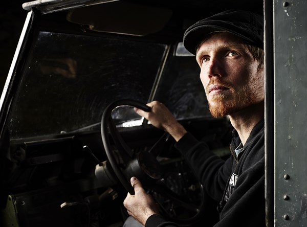 Man with a hat sitting in the driver's seat of an old car