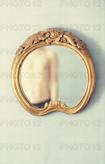 Shirtless adult male reflected in antique mirror hanging on wall