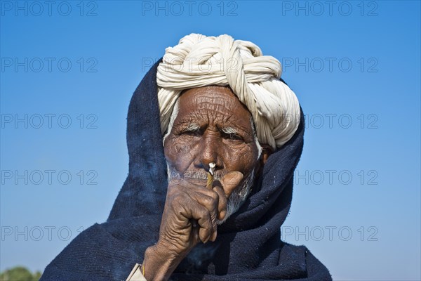 Indian man with a white turban smoking a bidi cigarette