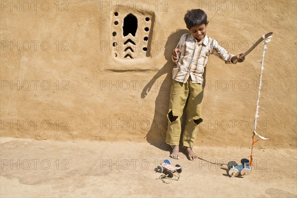 Boy playing with a home-made toy car outside a mud house
