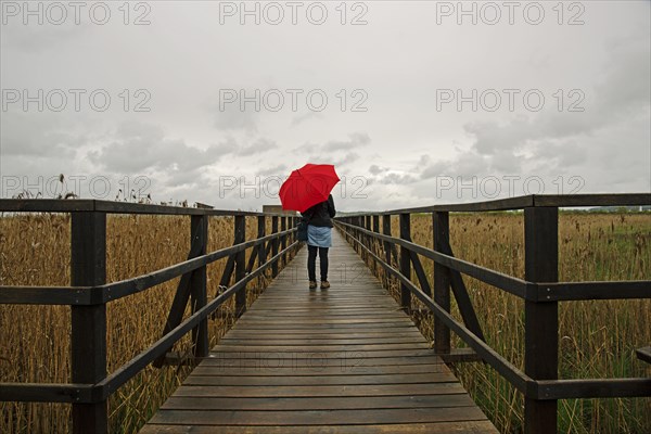 Woman holding a red umbrella while standing on a wooden pier