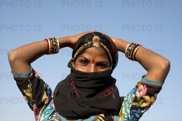 Young Indian woman with jewellery and a bindi covering her face with a black veil