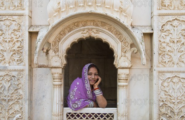 Young friendly Indian woman wearing a headscarf looking out of a window opening of an ornate marble facade