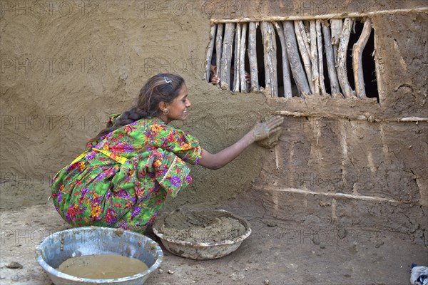 Girl in traditional dress plastering the wall of a house with a mixture of water