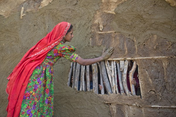 Girl in traditional dress plastering the wall of a house with a mixture of water