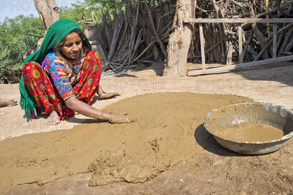 Woman in traditional dress plastering the floor of a courtyard with a mixture of water