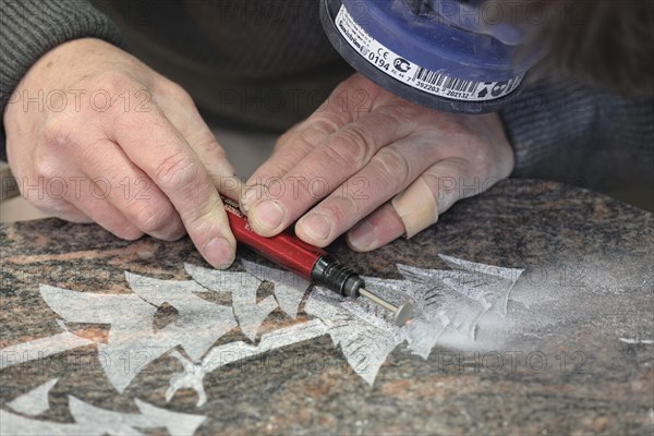 Sculptor with dust filter carving fir ornaments with a diamond grinder onto a grave stone