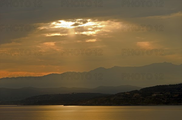 The rising sun forms sun beams behind the rocks of the island Ile de la Pietra near L'Île-Rousse. L'Île-Rousse  is in the department Haute-Corse