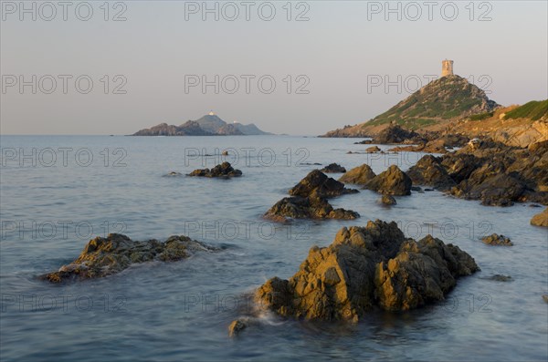 The genoese tower Tour de la Parata at the right and the islands Les Iles Sanguinaires behind the rocky mediterranean coast illuminated by warm morning light. Les Iles Sanguinaires are in the department Corse-du-Sud