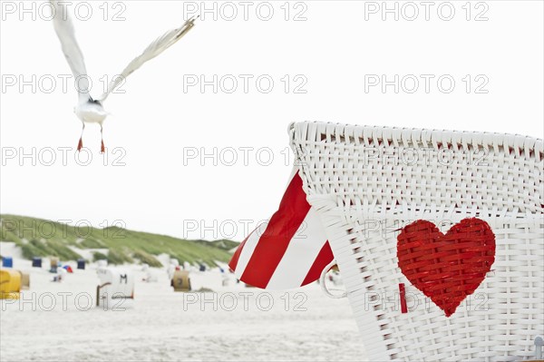 Roofed wicker beach chair with a red heart on the beach and a seagull in flight