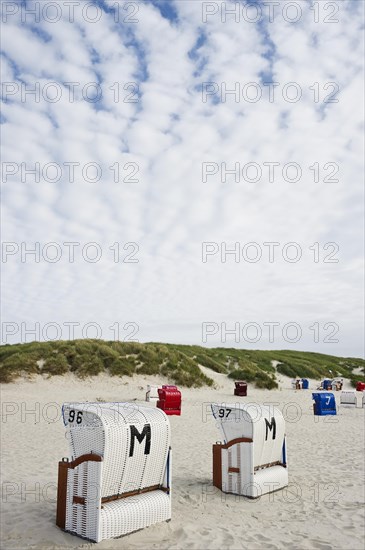 Roofed wicker beach chairs on the beach in front of sand dunes