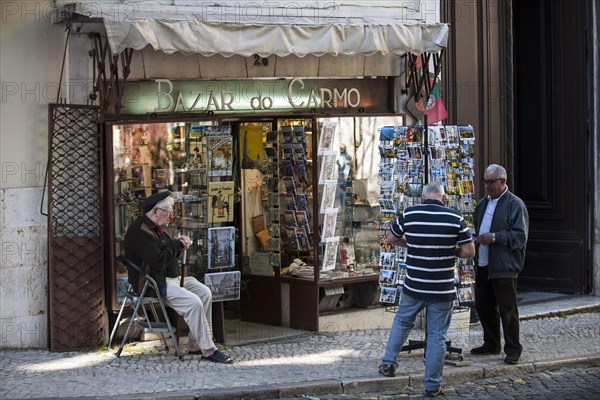 Souvenir vendor outside his shop with customers on the Largo do Carmo square