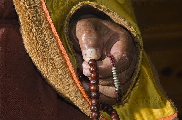 Hand of a monk praying and counting beads at a mala