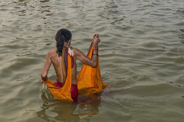 Woman wearing an orange sari taking a bath in the Sangam