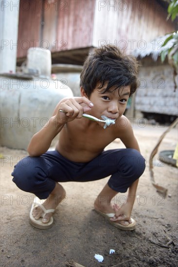 Young boy brushing his teeth outside a house