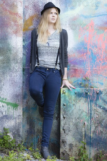 Young woman wearing a hat posing in front of a wall with graffiti